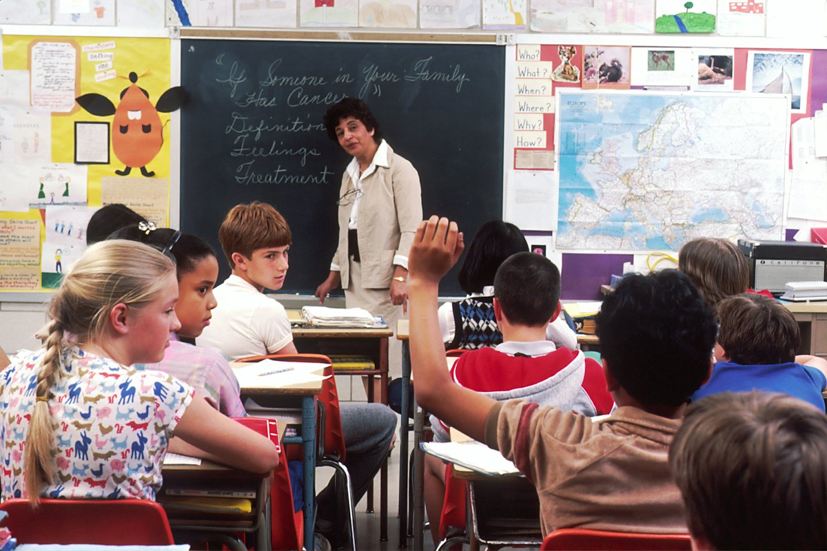A teacher and primary school children in front of a blackboard and map
