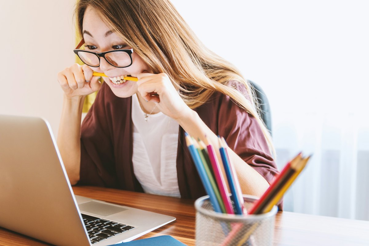 A student with a pencil in her mouth working at a laptop